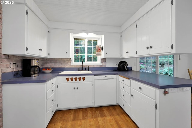 kitchen featuring dark countertops, dishwasher, a peninsula, and a sink