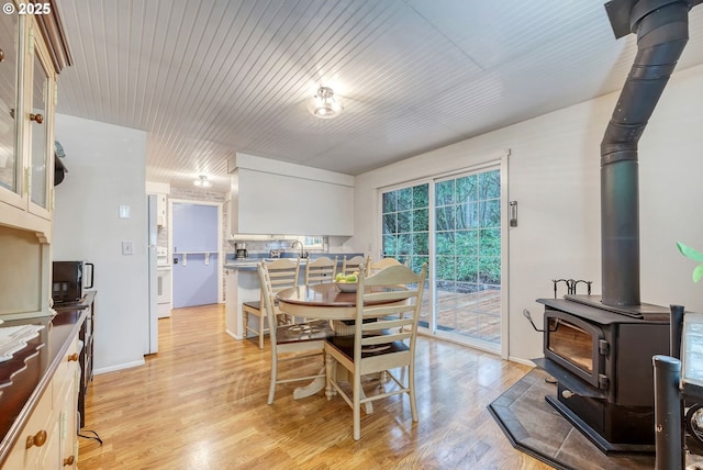 dining space featuring wooden ceiling, a wood stove, and light wood-style flooring