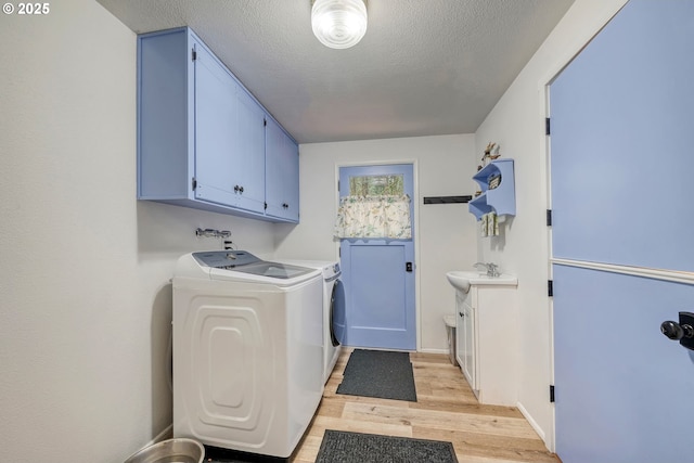 laundry area with washing machine and dryer, light wood-style floors, cabinet space, a textured ceiling, and a sink