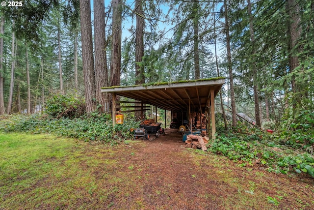 view of yard with a view of trees, an outbuilding, a detached carport, and an outdoor structure