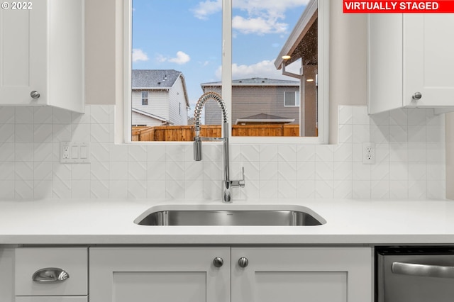 kitchen with decorative backsplash, white cabinetry, stainless steel dishwasher, and sink