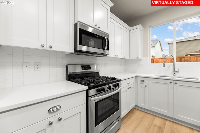 kitchen featuring white cabinets, sink, decorative backsplash, light wood-type flooring, and appliances with stainless steel finishes