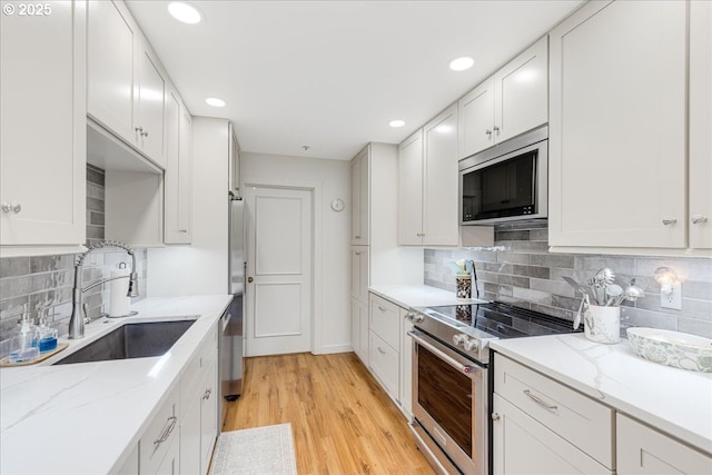 724 NW Westover Cir, Portland, OR 97210 - kitchen featuring appliances with stainless steel finishes, a sink, white cabinets, light wood finished floors, and decorative backsplash