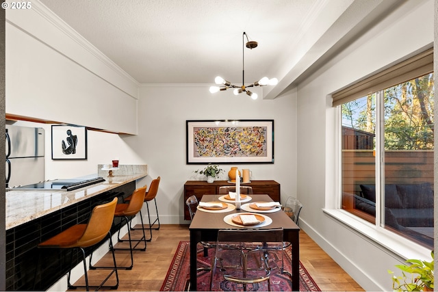 dining space with light wood-type flooring, baseboards, a chandelier, and crown molding