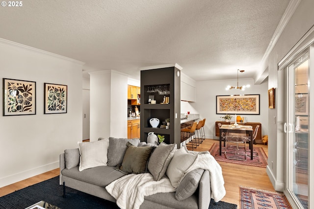 living area featuring light wood-type flooring, a textured ceiling, an inviting chandelier, and crown molding