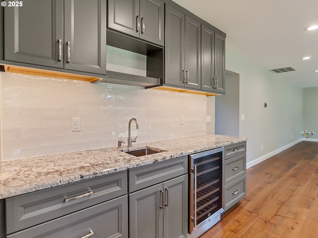 kitchen featuring beverage cooler, a sink, light wood-type flooring, visible vents, and baseboards