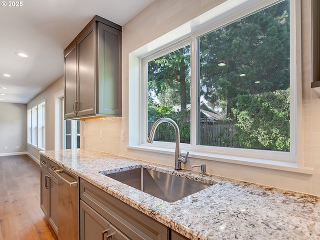kitchen with light stone countertops, recessed lighting, stainless steel dishwasher, light wood finished floors, and a sink