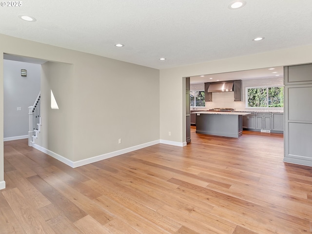 unfurnished living room with stairs, light wood-style flooring, baseboards, and recessed lighting