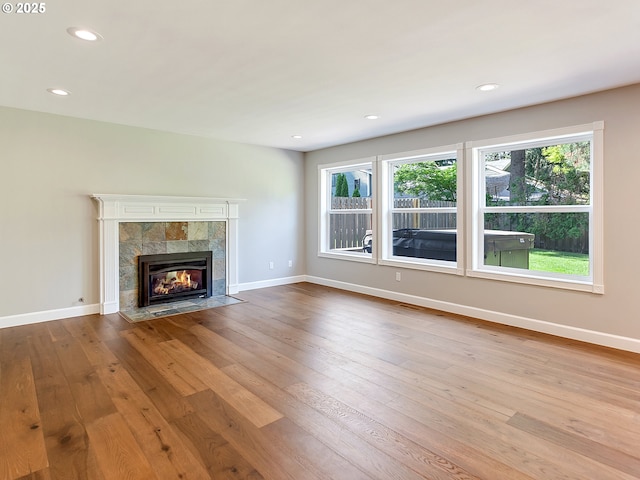 unfurnished living room with a tiled fireplace, baseboards, wood-type flooring, and recessed lighting