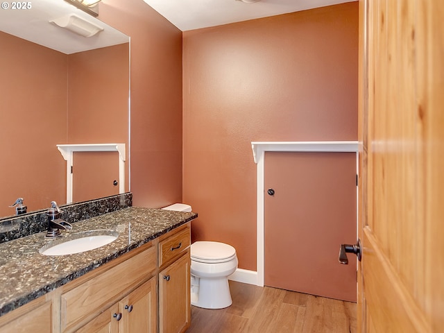 half bath with toilet, baseboards, vanity, and wood finished floors