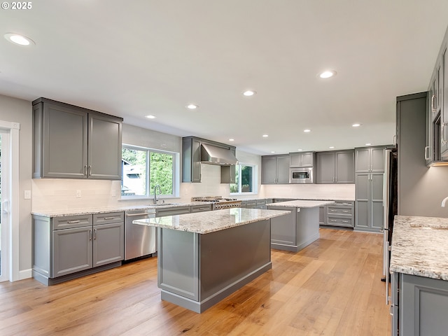 kitchen with a kitchen island, gray cabinets, stainless steel appliances, and wall chimney exhaust hood