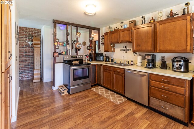 kitchen featuring sink, stainless steel appliances, light hardwood / wood-style floors, and brick wall