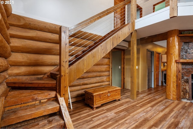 stairs with rustic walls, a stone fireplace, wood finished floors, and a towering ceiling