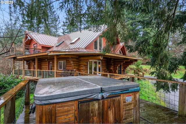 rear view of property featuring a hot tub, a wooden deck, log exterior, a standing seam roof, and metal roof