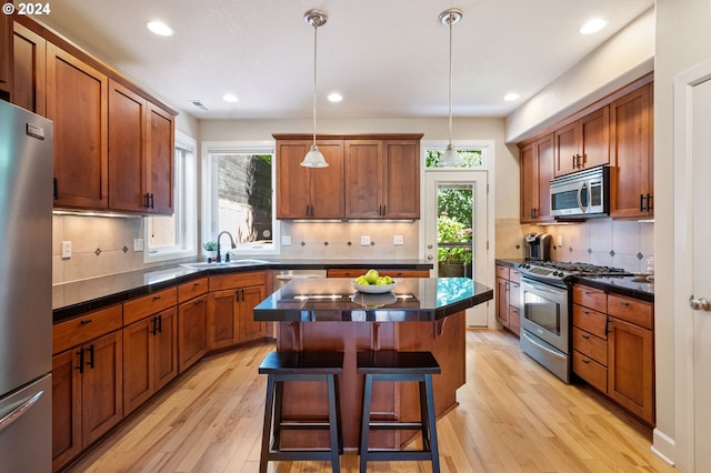 kitchen featuring pendant lighting, appliances with stainless steel finishes, backsplash, a center island, and a breakfast bar area