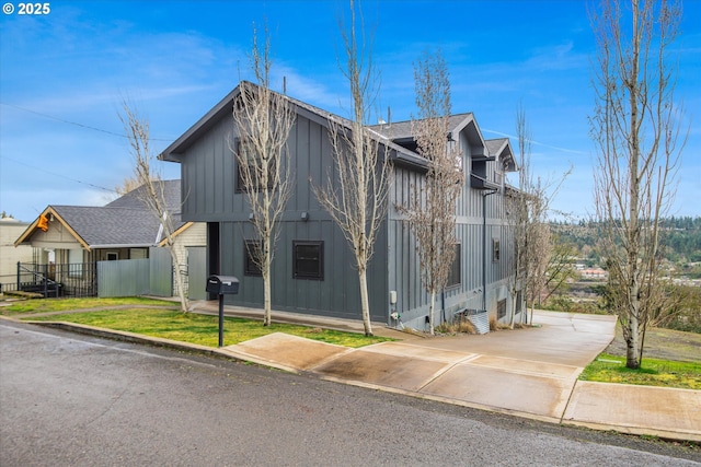 view of front facade featuring a shingled roof, fence, board and batten siding, and a front yard