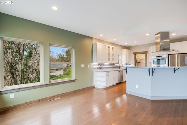 kitchen with a breakfast bar, island exhaust hood, stainless steel appliances, light wood-style flooring, and white cabinets