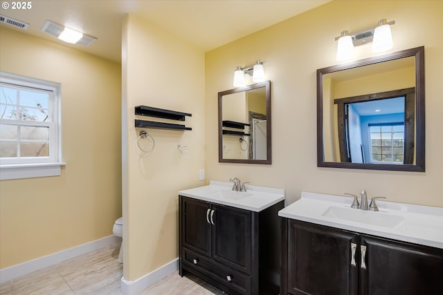 full bath featuring baseboards, visible vents, two vanities, and a sink