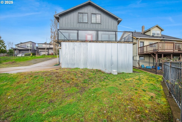 rear view of house with board and batten siding, fence, a lawn, and an outbuilding