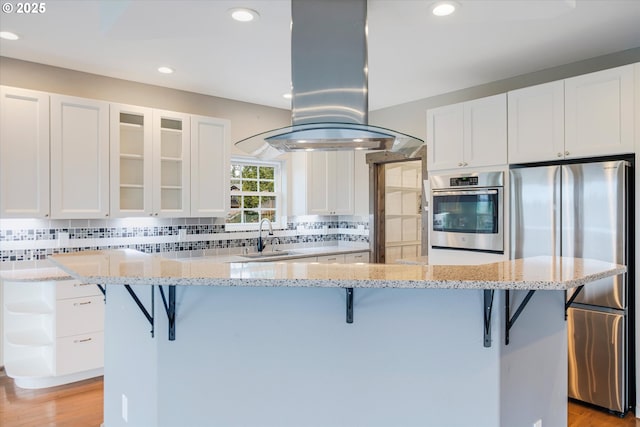 kitchen featuring a breakfast bar, tasteful backsplash, appliances with stainless steel finishes, white cabinets, and island range hood