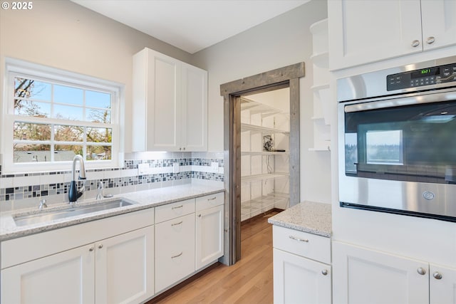 kitchen featuring light stone counters, light wood finished floors, decorative backsplash, white cabinets, and a sink