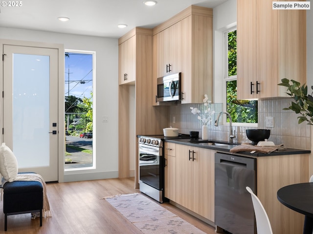 207 NE Going St Unit 3, Portland, OR 97211 - kitchen featuring appliances with stainless steel finishes, dark countertops, light brown cabinetry, tasteful backsplash, and light wood-type flooring