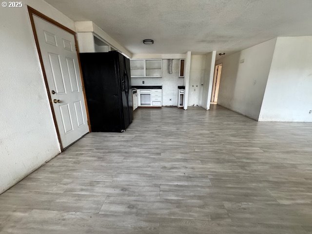 interior space with a textured ceiling, black refrigerator with ice dispenser, wood finished floors, and open floor plan