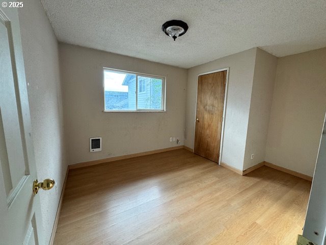 unfurnished bedroom with a textured ceiling, baseboards, a closet, light wood-type flooring, and heating unit