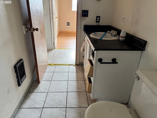 bathroom featuring heating unit, a textured wall, toilet, a sink, and tile patterned flooring