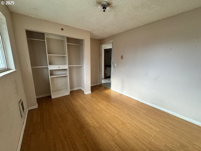 unfurnished bedroom featuring a closet, a textured ceiling, baseboards, and wood finished floors