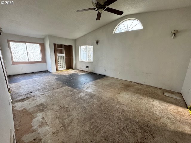 spare room with a ceiling fan, vaulted ceiling, and a textured ceiling