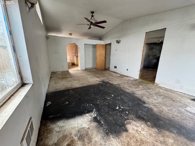 unfurnished living room featuring a ceiling fan, arched walkways, visible vents, and vaulted ceiling