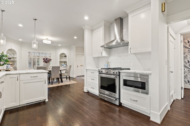 kitchen featuring appliances with stainless steel finishes, pendant lighting, white cabinetry, dark wood-type flooring, and wall chimney range hood