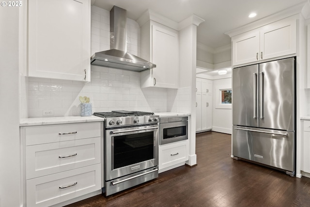 kitchen with white cabinetry, backsplash, stainless steel appliances, dark wood-type flooring, and wall chimney range hood