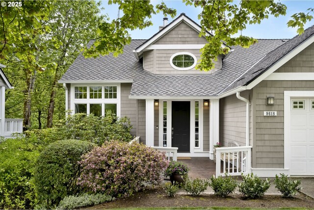 view of front facade with roof with shingles, covered porch, and a garage