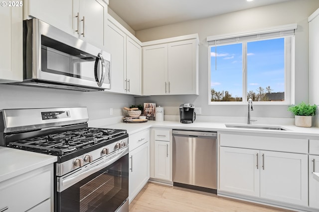 kitchen with white cabinets, light wood-style flooring, stainless steel appliances, light countertops, and a sink