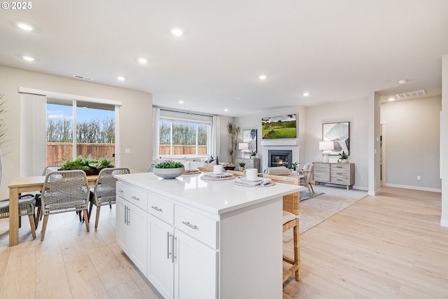 kitchen featuring a center island, recessed lighting, light wood-style flooring, a glass covered fireplace, and white cabinets