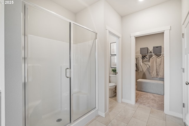 bathroom with a walk in closet, toilet, a stall shower, tile patterned flooring, and baseboards