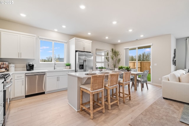 kitchen with light wood finished floors, appliances with stainless steel finishes, a kitchen bar, and a sink