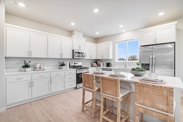 kitchen featuring stainless steel appliances, light countertops, white cabinets, light wood-type flooring, and a kitchen breakfast bar