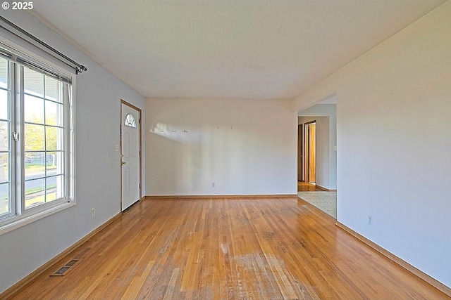 empty room featuring baseboards, visible vents, a healthy amount of sunlight, and light wood-style flooring