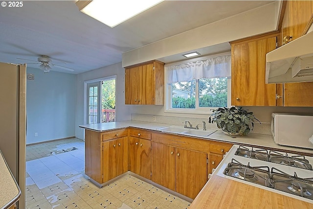 kitchen featuring a sink, a peninsula, light countertops, under cabinet range hood, and a ceiling fan
