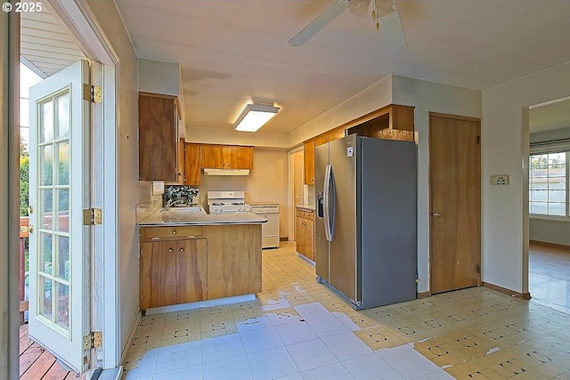 kitchen with brown cabinets, stainless steel fridge with ice dispenser, a ceiling fan, white range with gas stovetop, and under cabinet range hood