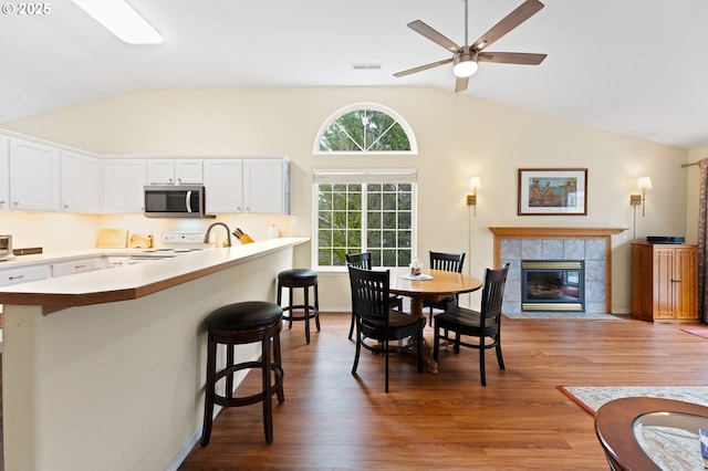 dining area featuring visible vents, a tiled fireplace, lofted ceiling, wood finished floors, and a ceiling fan