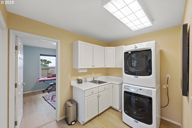 laundry room featuring cabinets, stacked washing maching and dryer, sink, and light hardwood / wood-style flooring