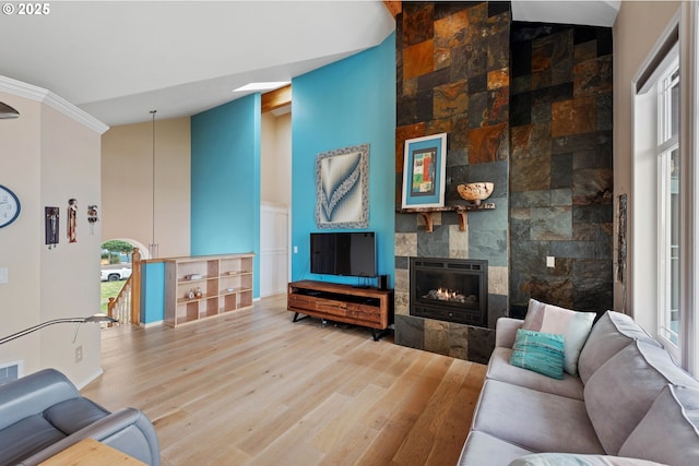 living room with a tile fireplace, hardwood / wood-style floors, high vaulted ceiling, and ornamental molding