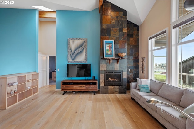 living room with high vaulted ceiling, a tile fireplace, and light hardwood / wood-style flooring