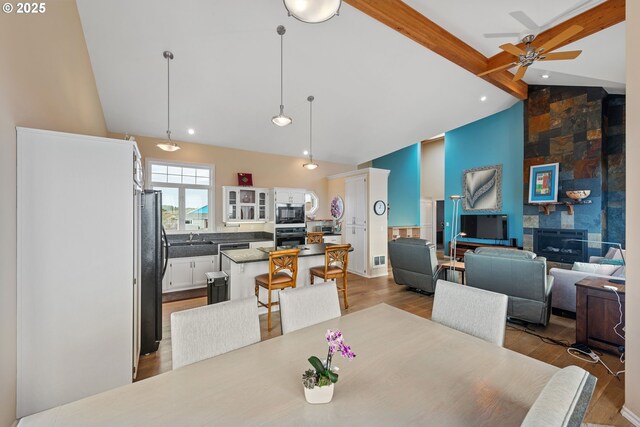 dining area with lofted ceiling with beams, sink, ceiling fan, a fireplace, and light hardwood / wood-style floors