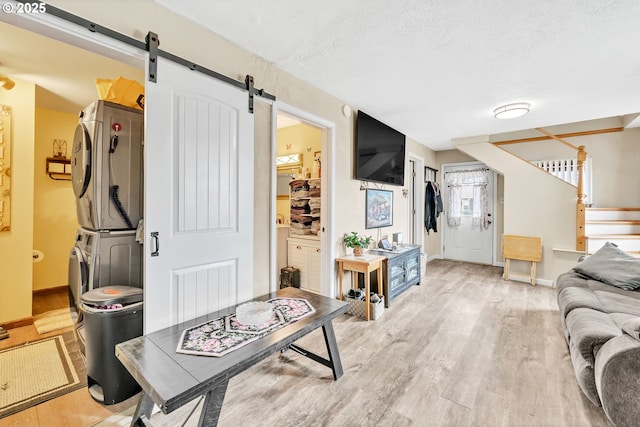 living area with stairway, a barn door, a textured ceiling, stacked washing maching and dryer, and light wood-type flooring