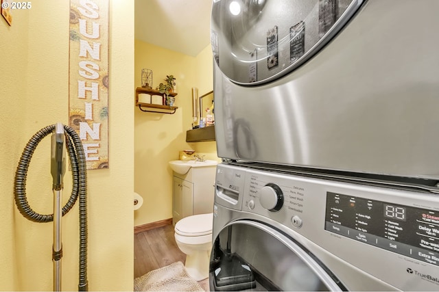 clothes washing area featuring stacked washer and dryer, a sink, wood finished floors, laundry area, and baseboards